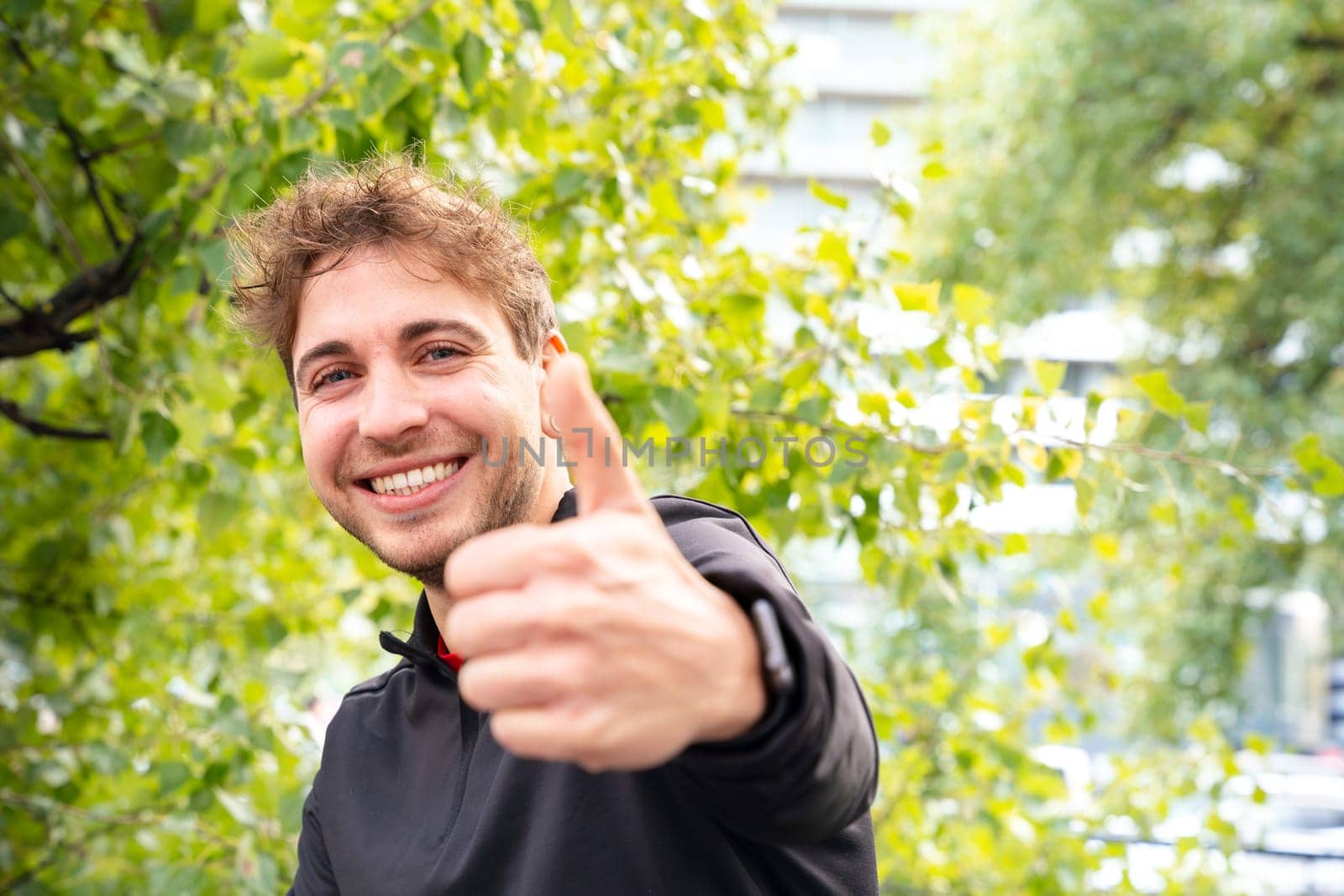 Smiling sporty man with showing finger up looking at camera outdoors. by molesjuny