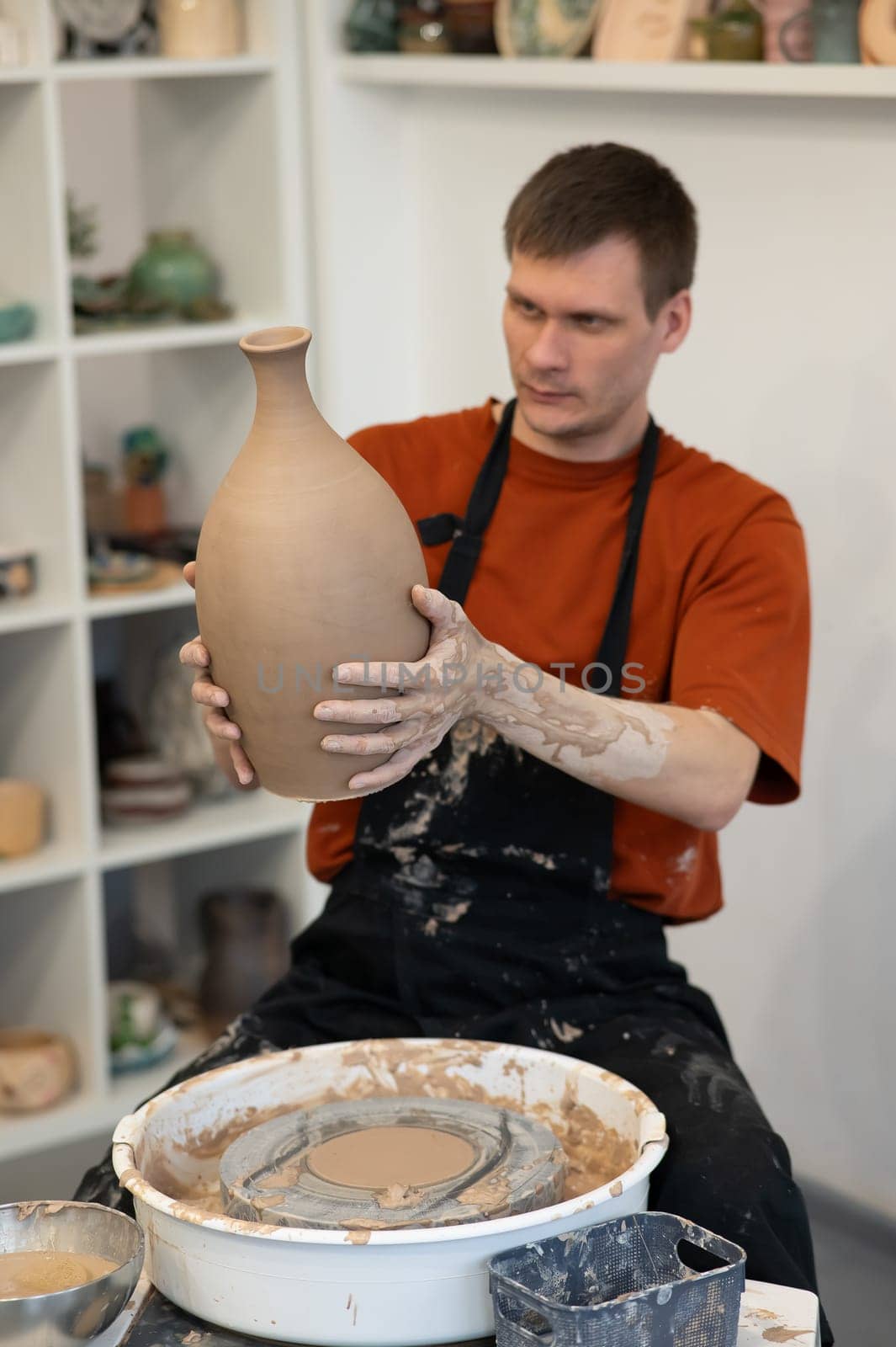 A man makes a ceramic vase on a pottery wheel. Vertical photo. by mrwed54