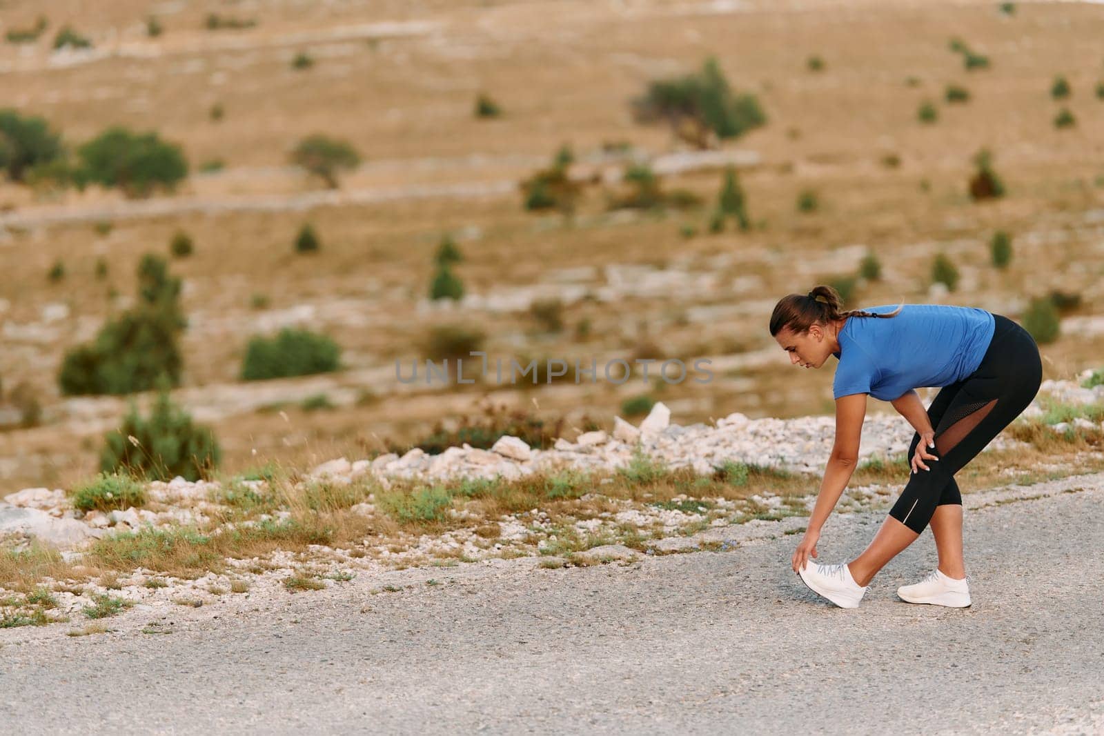 A determined female athlete stretches her muscles after a strenuous run through rugged mountain terrain, surrounded by breathtaking rocky landscapes.