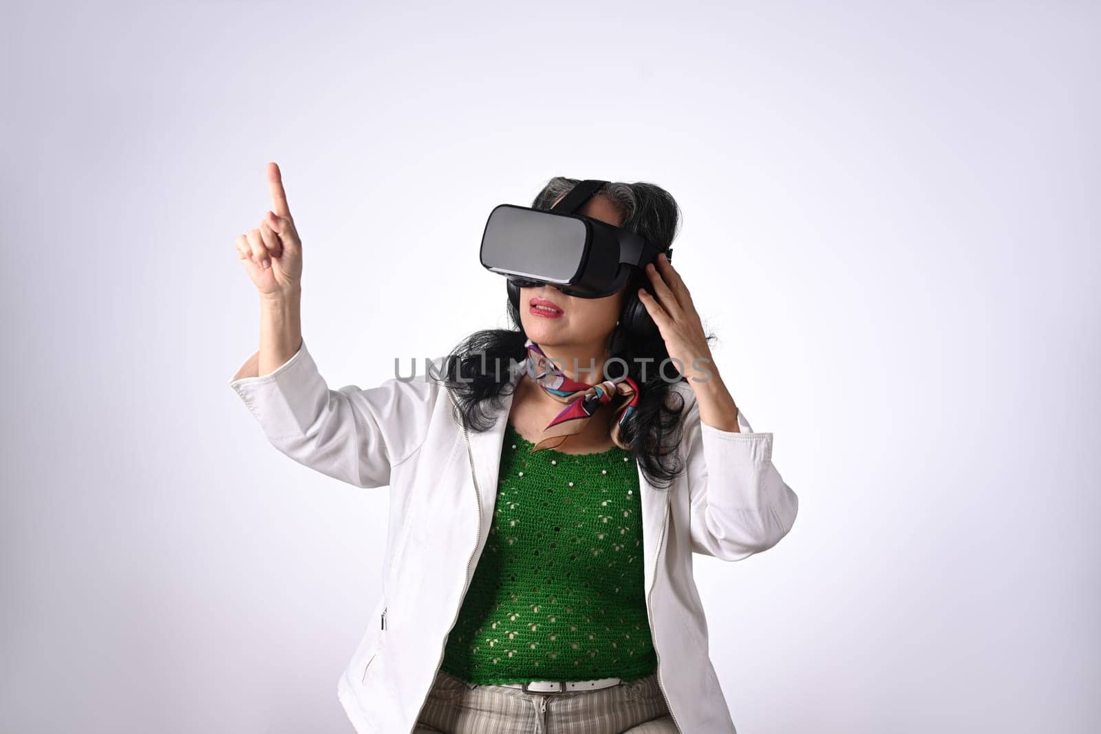 Elderly senior woman wearing VR headset enjoying virtual reality experience isolated on white background.