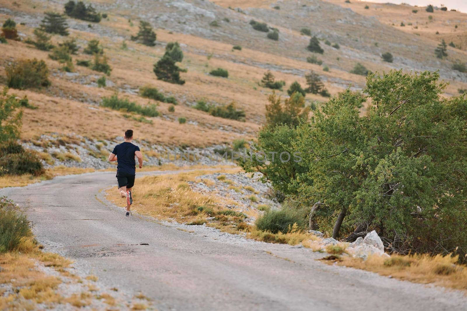 A muscular male athlete runs along a rugged mountain path at sunrise, surrounded by breathtaking rocky landscapes and natural beauty.