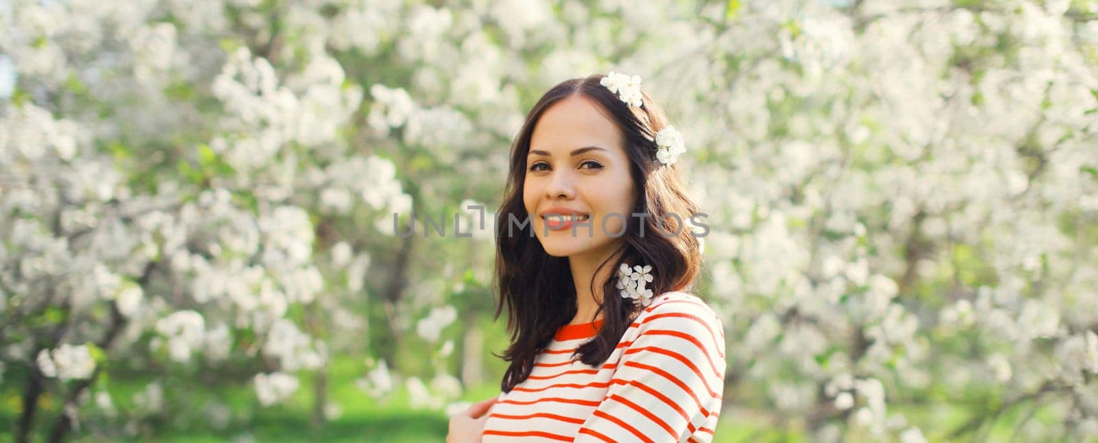 Portrait of lovely happy smiling young woman in spring blooming garden with white flowers on the trees in park