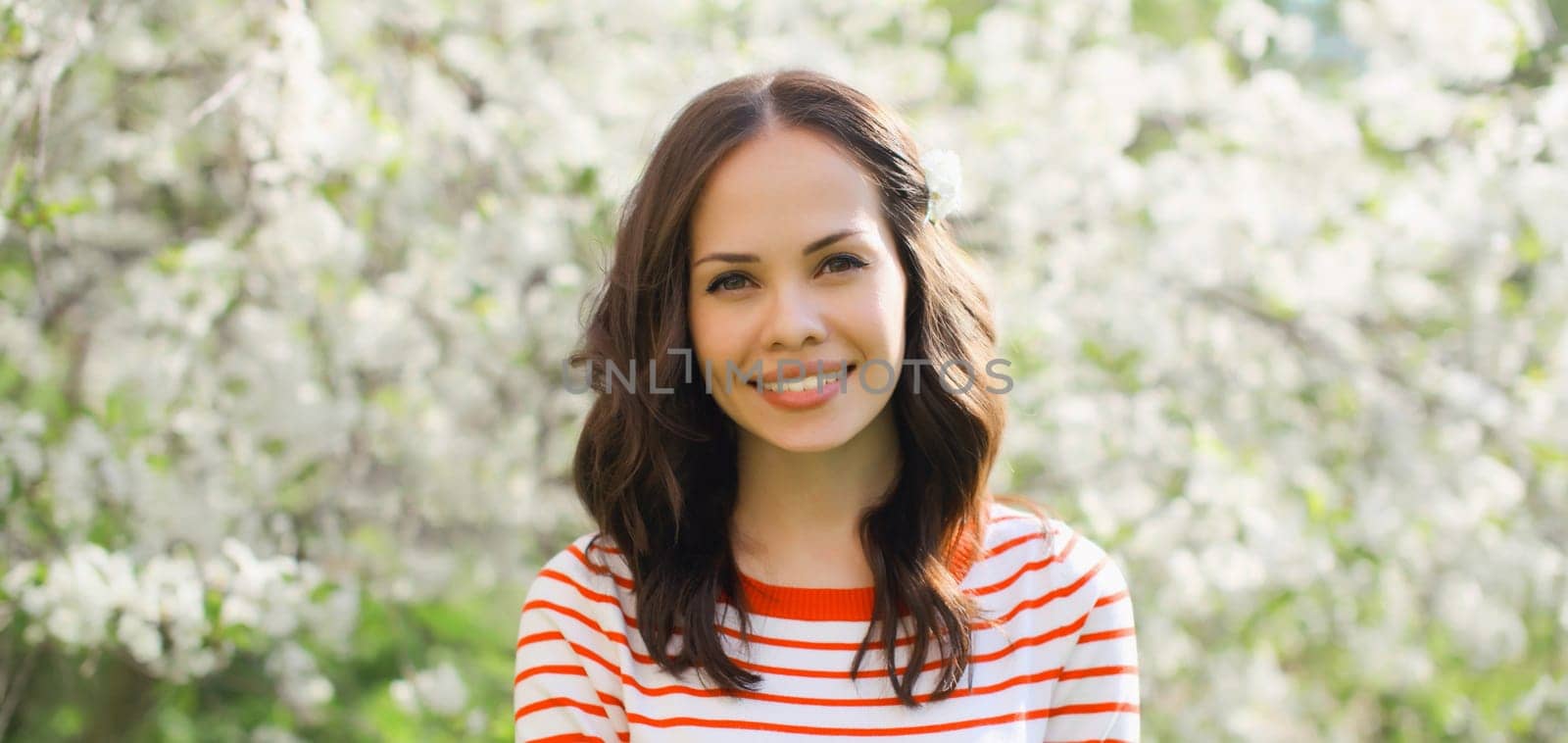 Portrait of lovely happy smiling young woman in spring blooming garden with white flowers on the trees in park