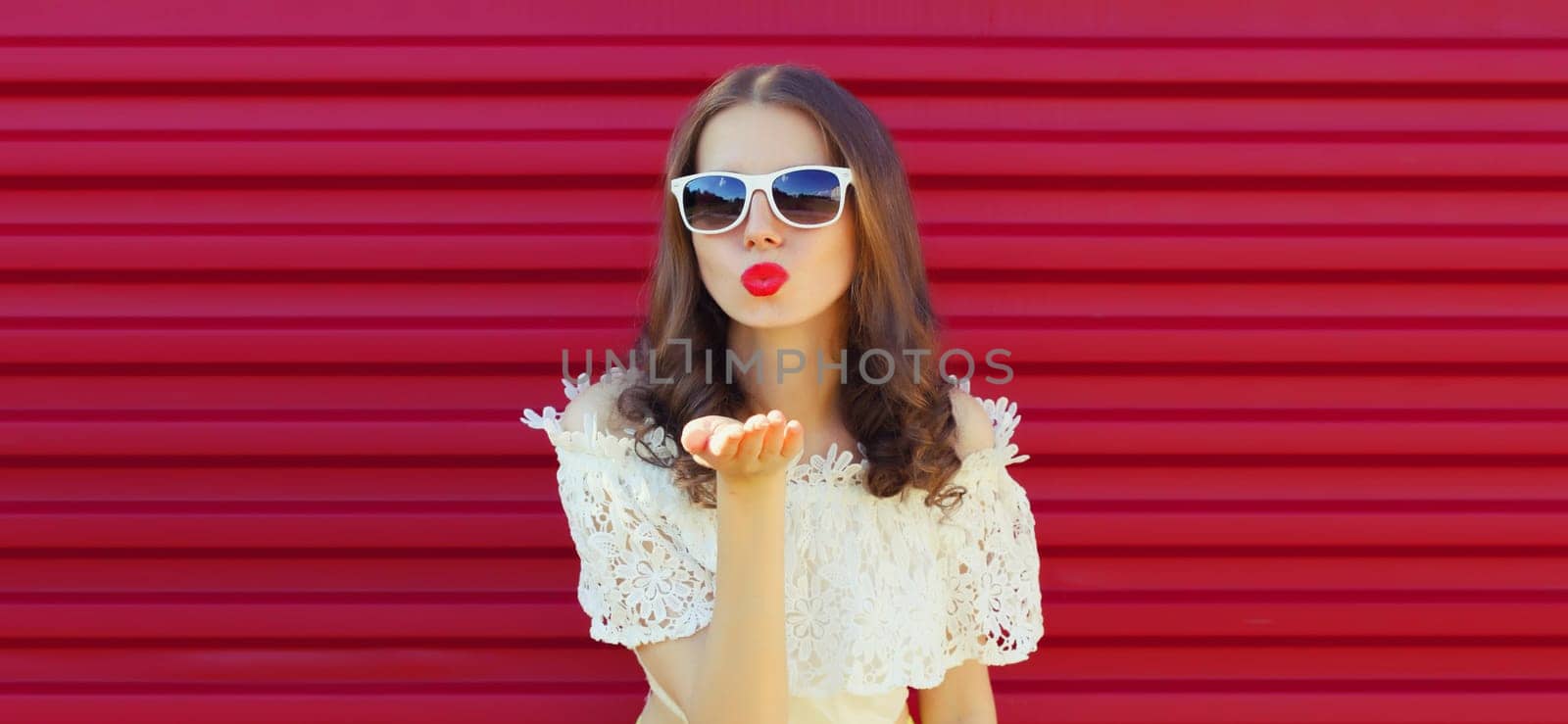 Portrait of beautiful young woman model blowing kiss wearing a white glasses posing on pink background