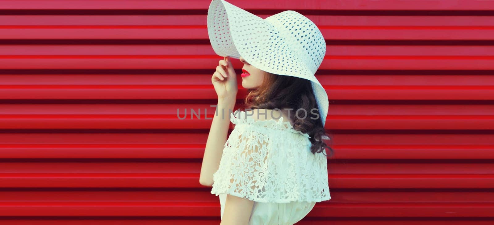 Beautiful young woman model posing in white summer straw hat on pink background