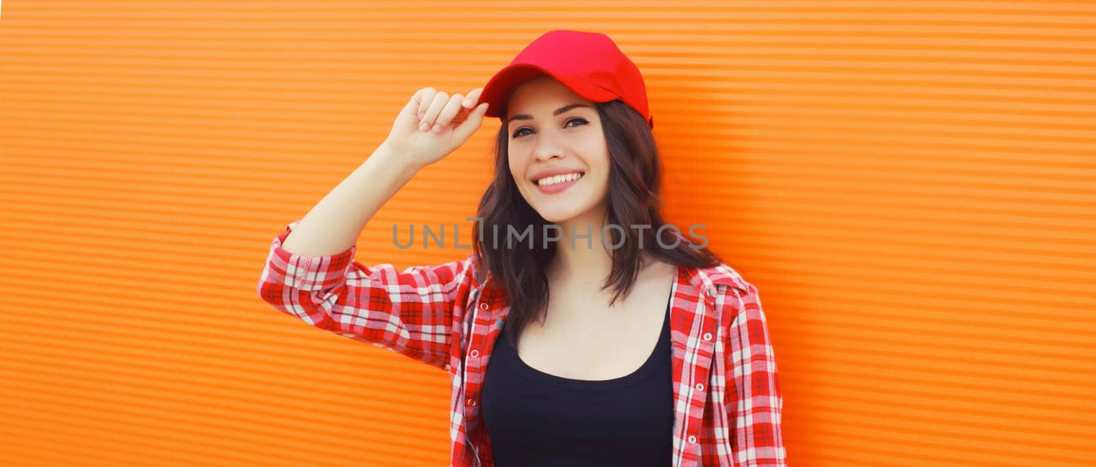 Summer portrait of happy smiling young woman posing in red baseball cap, casual clothes on city street