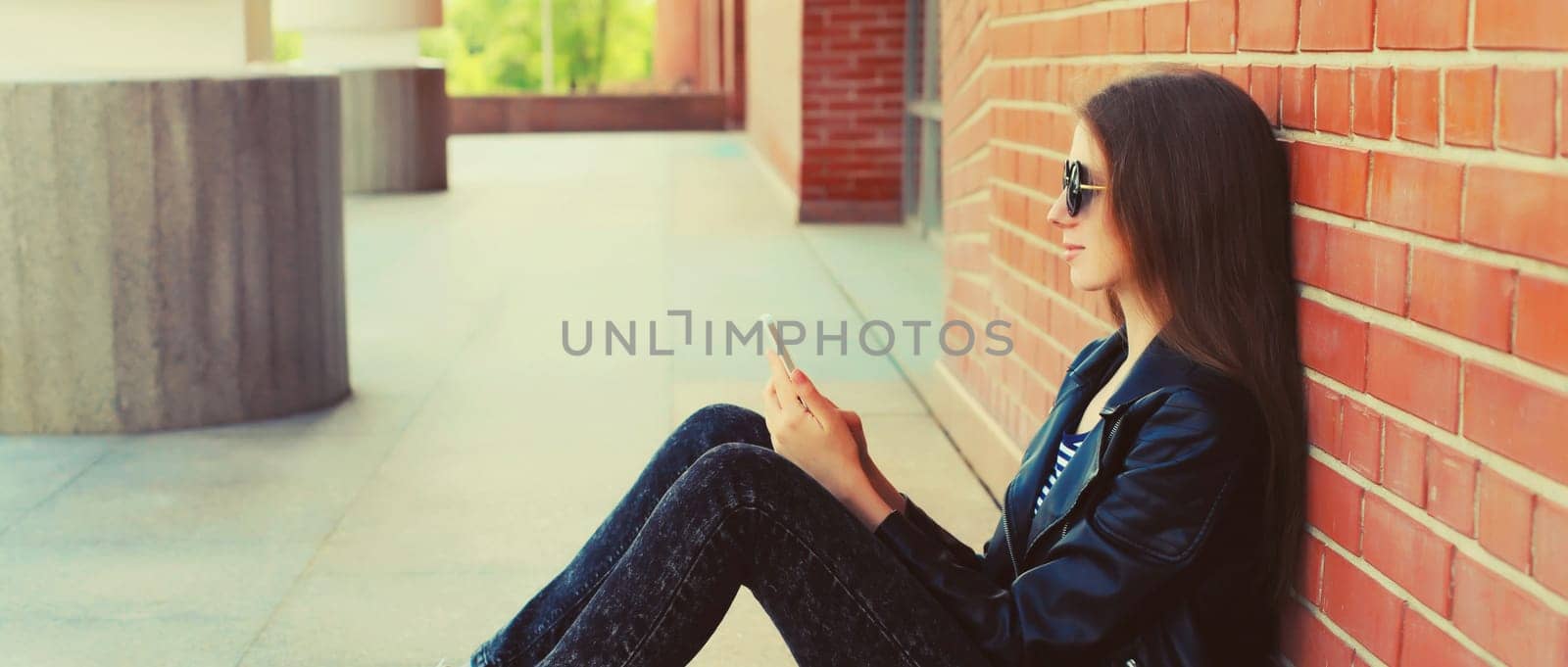 Modern caucasian young woman 20s with mobile phone looking at device on city street by Rohappy