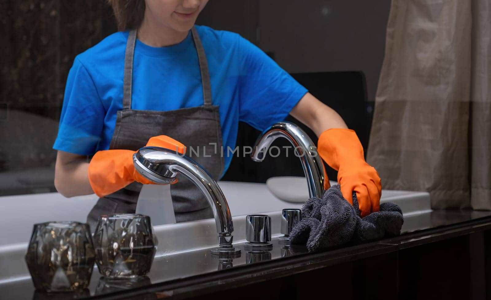 Housekeeper cleaning bathroom sink with orange gloves. Concept of cleanliness and hygiene.