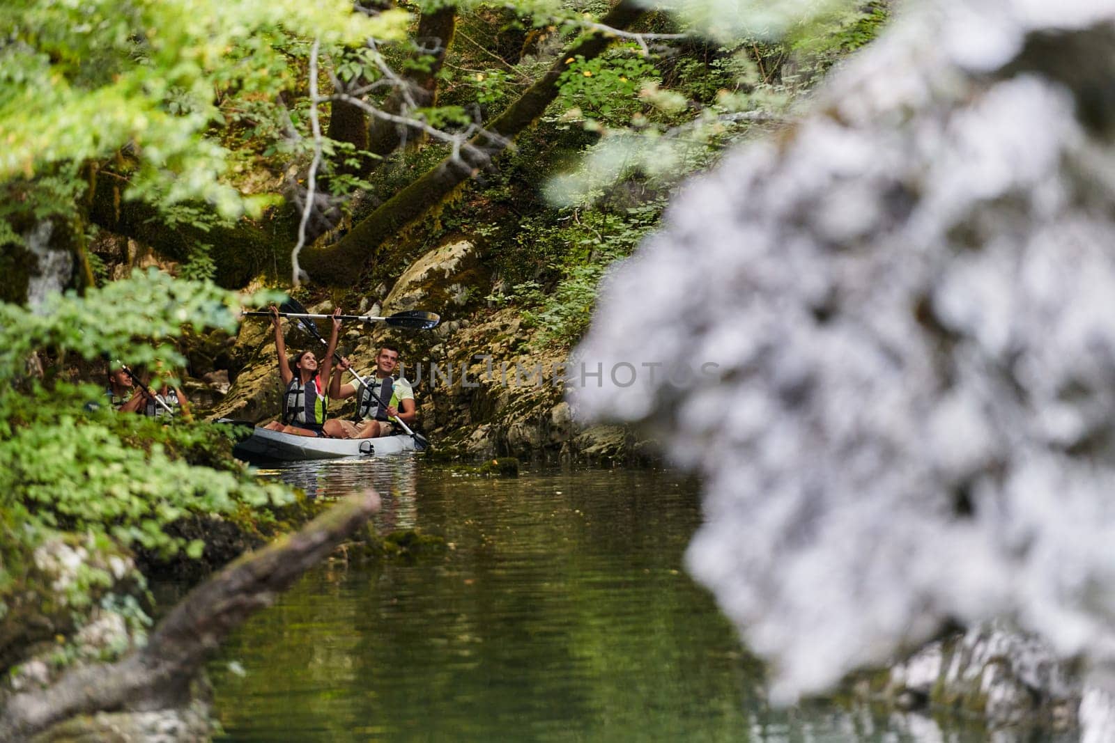 A young couple enjoying an idyllic kayak ride in the middle of a beautiful river surrounded by forest greenery.