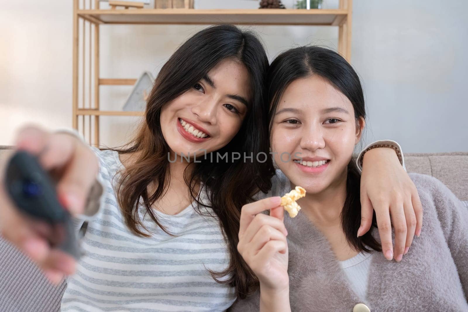 Close up two young women watching TV and eating popcorn on couch. Concept of relaxation and friendship by wichayada