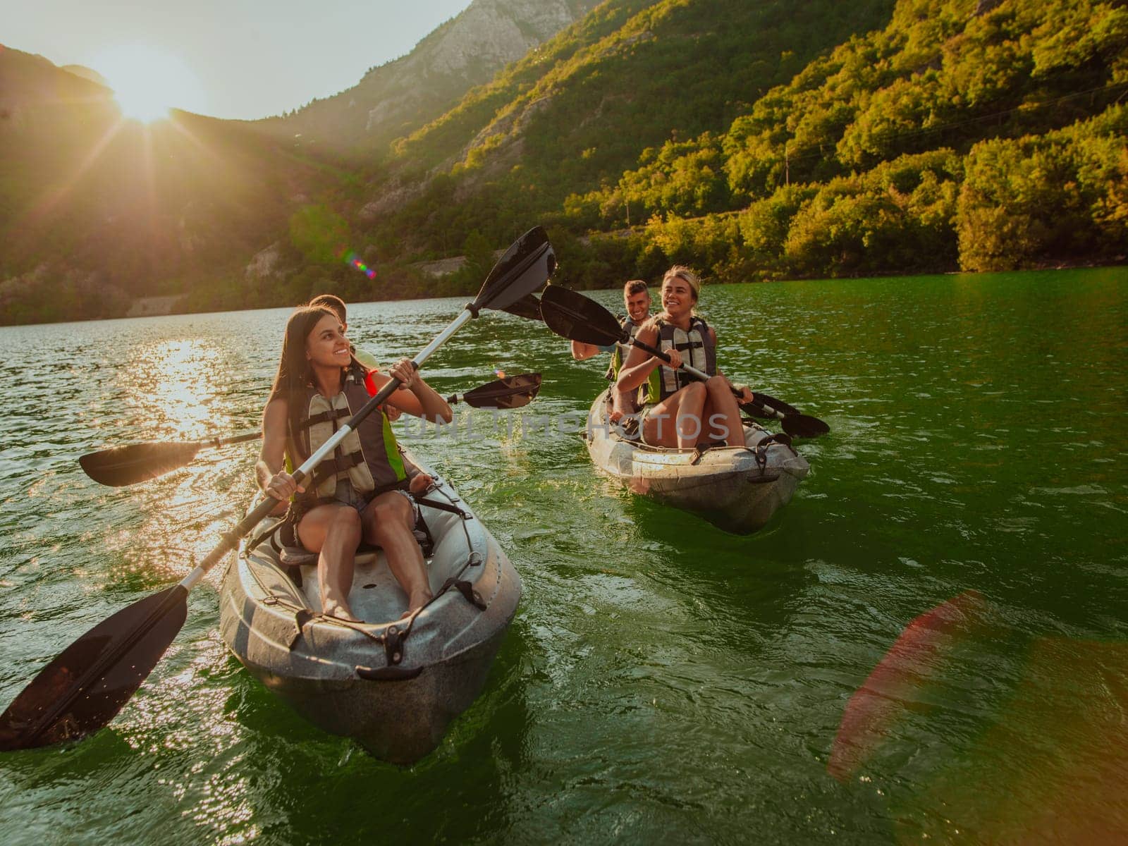 A group of friends enjoying fun and kayaking exploring the calm river, surrounding forest and large natural river canyons during an idyllic sunset