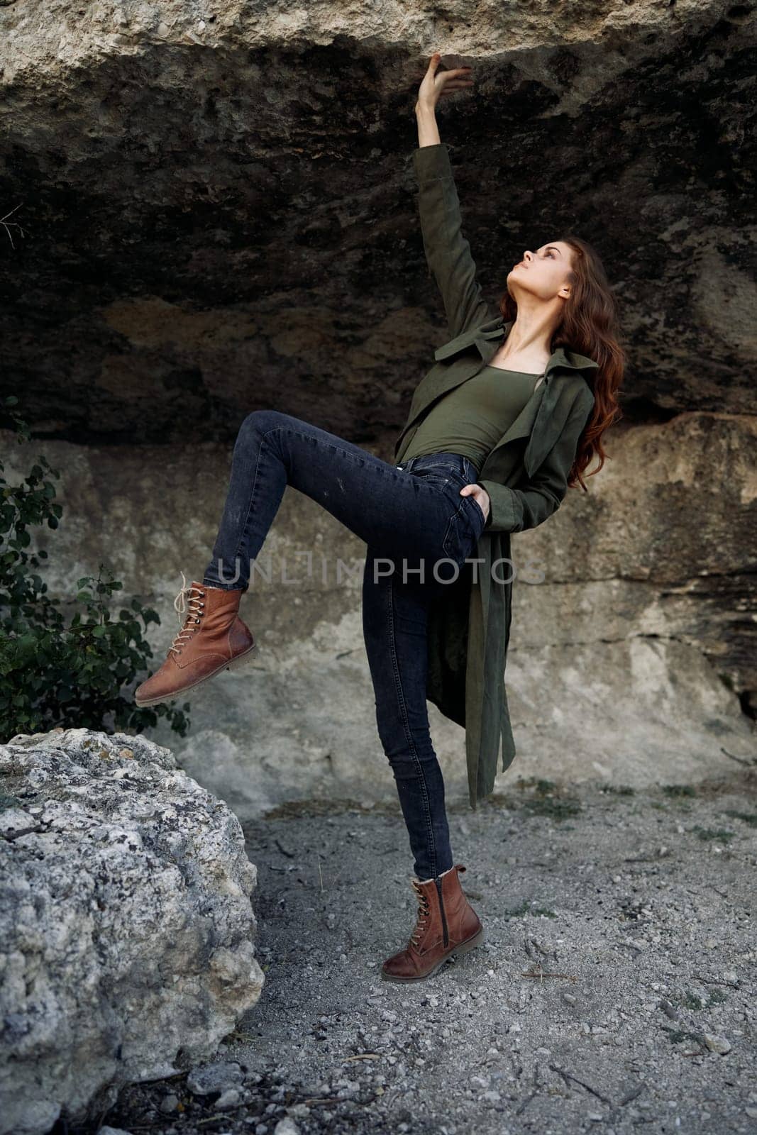 Woman standing on rock in forest wearing green coat and jeans