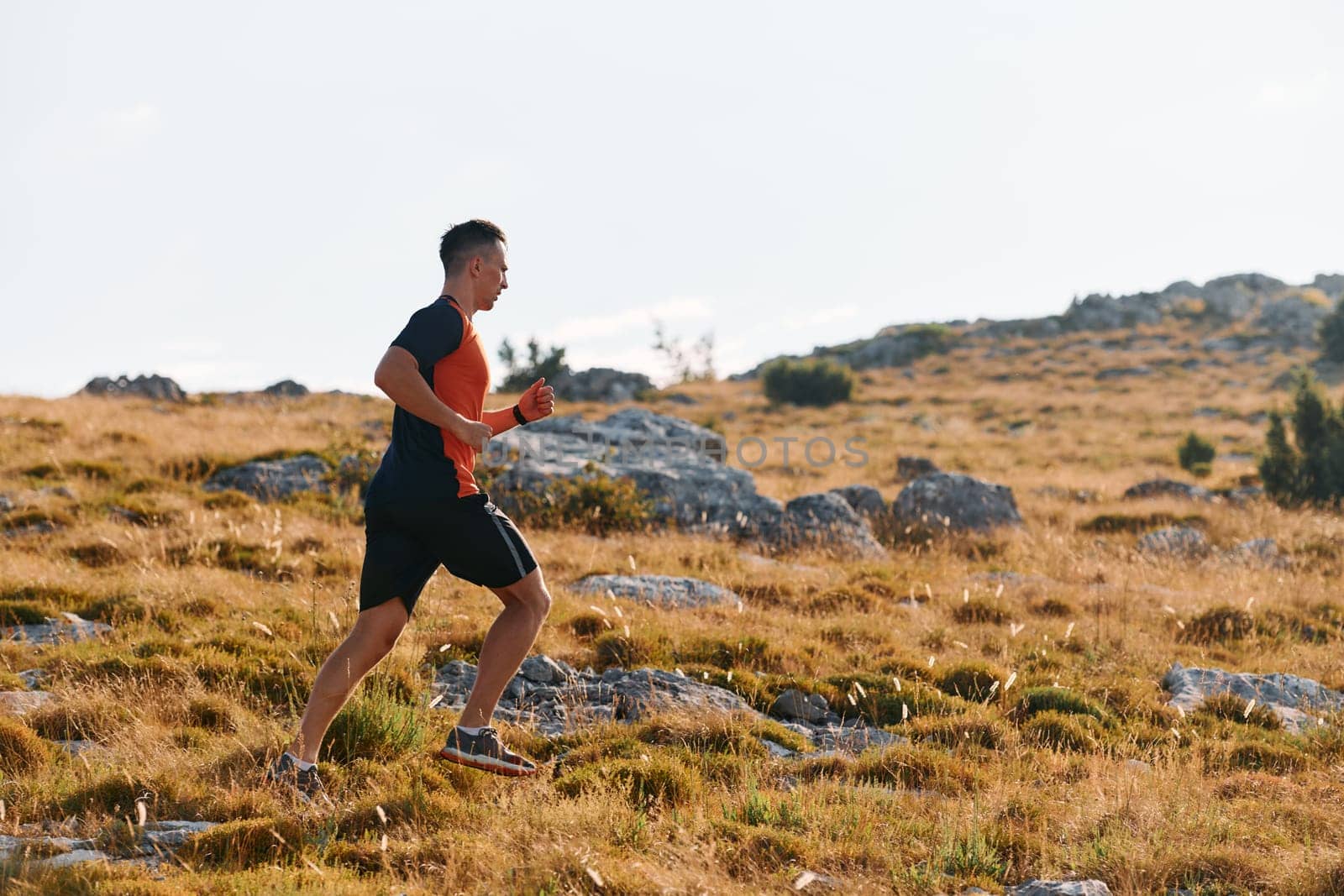 A muscular male athlete runs along a rugged mountain path at sunrise, surrounded by breathtaking rocky landscapes and natural beauty.