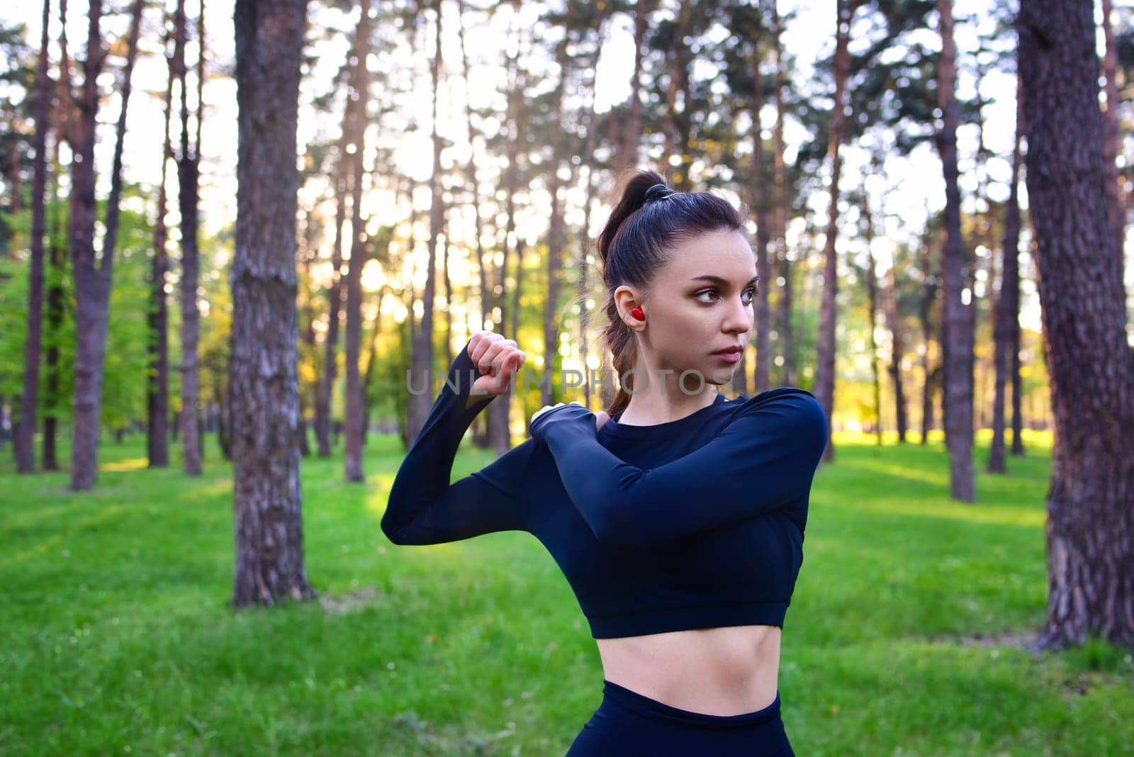 A young woman in a sports top warming up for a sport in the park. by Nickstock