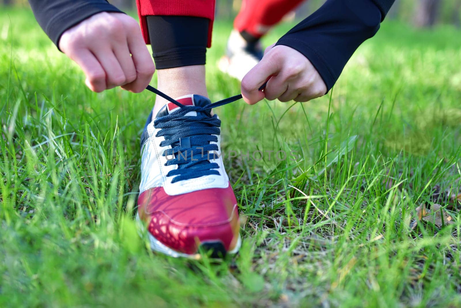 A woman ties the laces on her sneakers in the park. by Nickstock