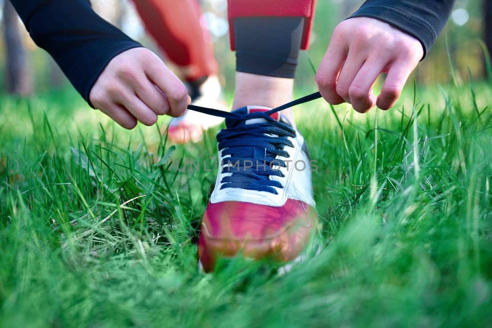 A woman tightens the laces on her athletic sneakers in a park while jogging. by Nickstock