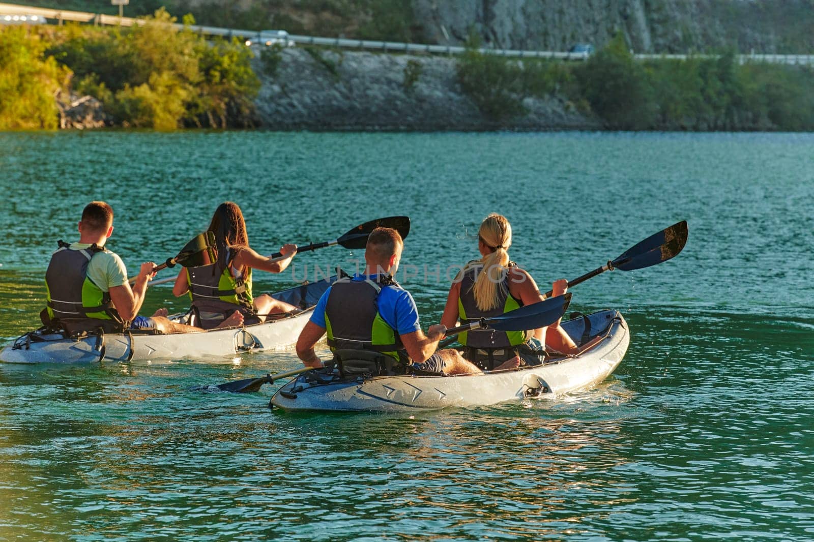 A group of friends enjoying fun and kayaking exploring the calm river, surrounding forest and large natural river canyons during an idyllic sunset