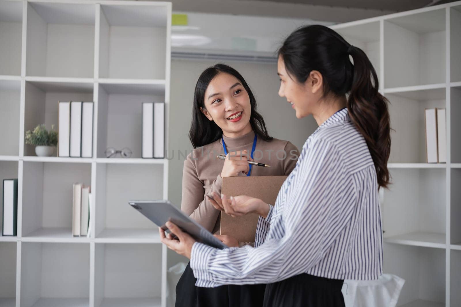 Two businesswomen discussing project with tablet in modern office. Concept of professional collaboration and teamwork by wichayada