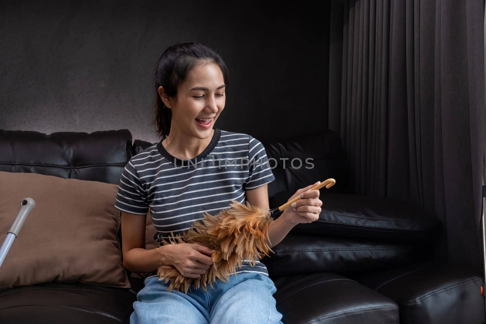Smiling woman holding feather duster in living room. Concept of household chores and cleanliness.