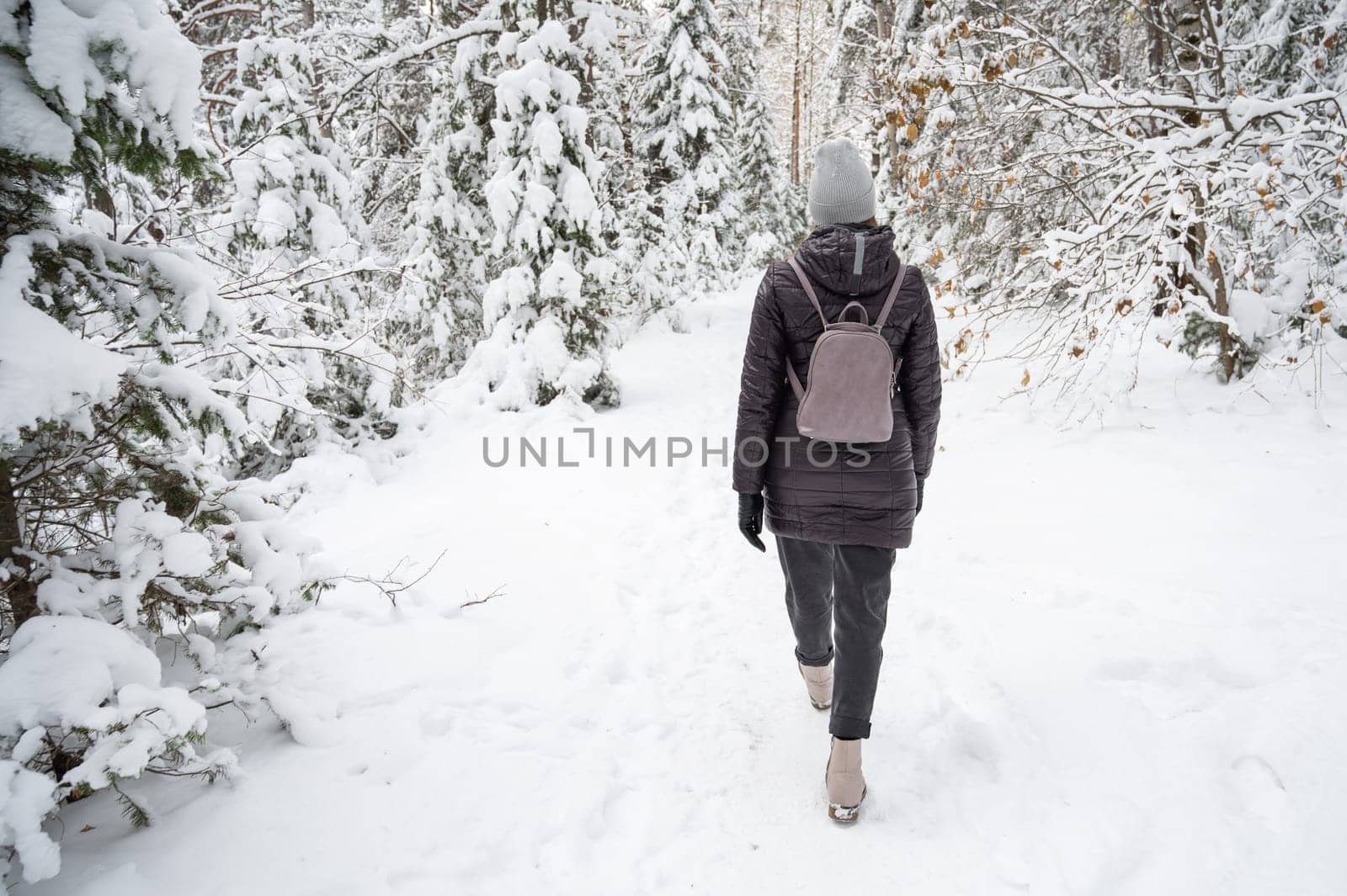 Woman in winter jacket walking in snowy winter forest, snowy winter day