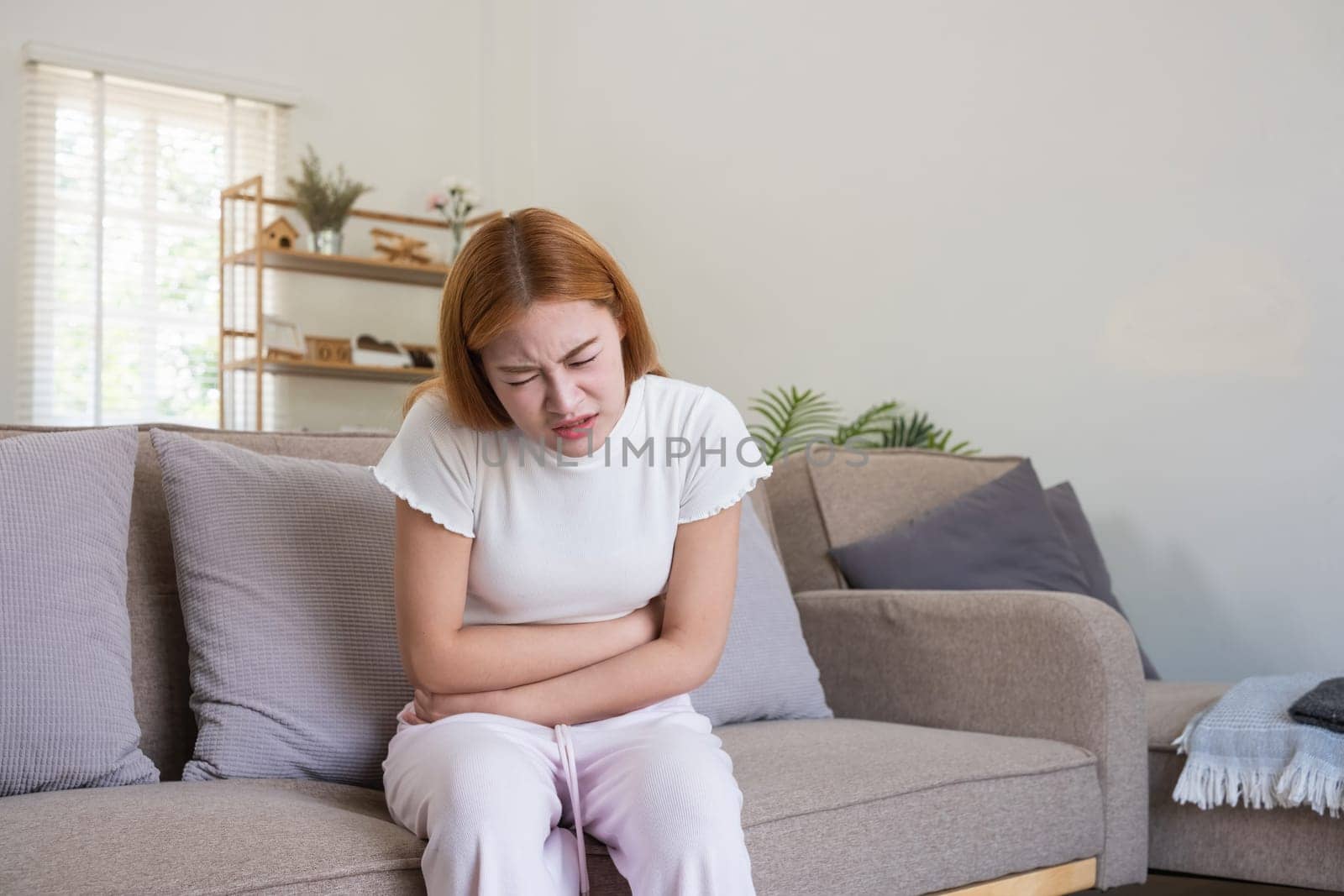 Young Asian Woman Suffering from Stomach Pain on Sofa by wichayada