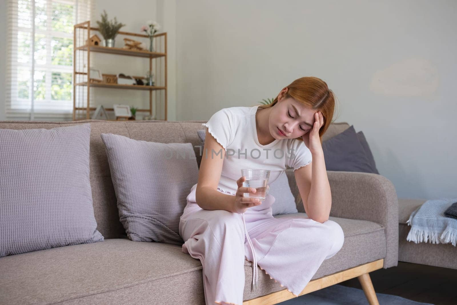 Asian woman feeling stressed and holding glass of water at home. Concept of mental health, stress, and anxiety by wichayada