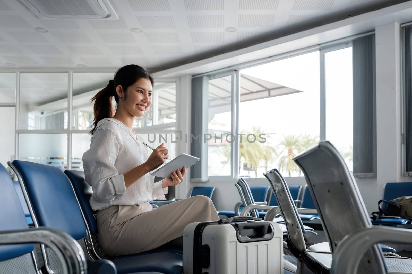Young woman waiting at airport with luggage and tablet. Concept of travel and technology.