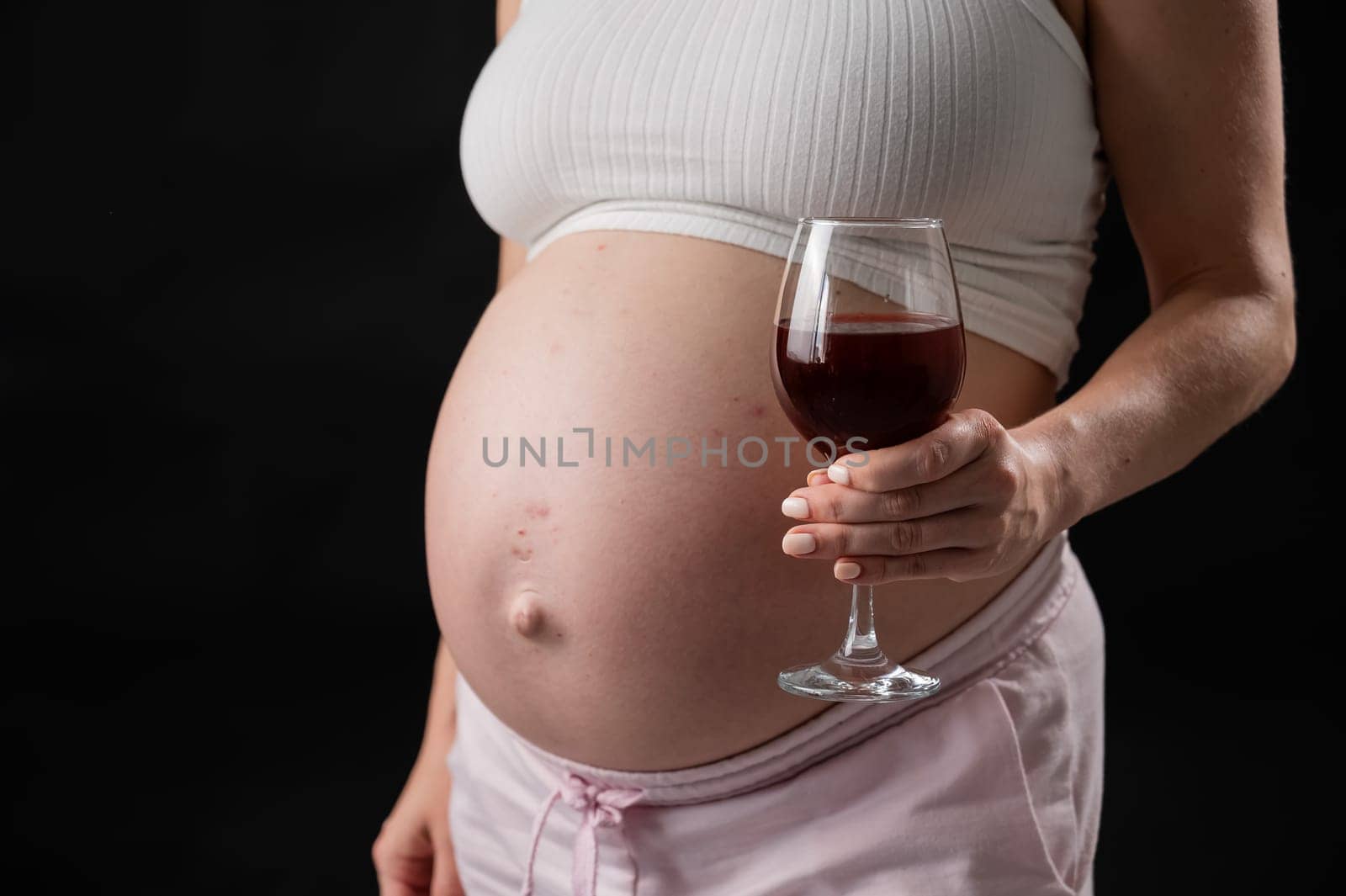 Close-up of the belly of a pregnant woman holding a glass of red wine on a black background. Copy space. by mrwed54