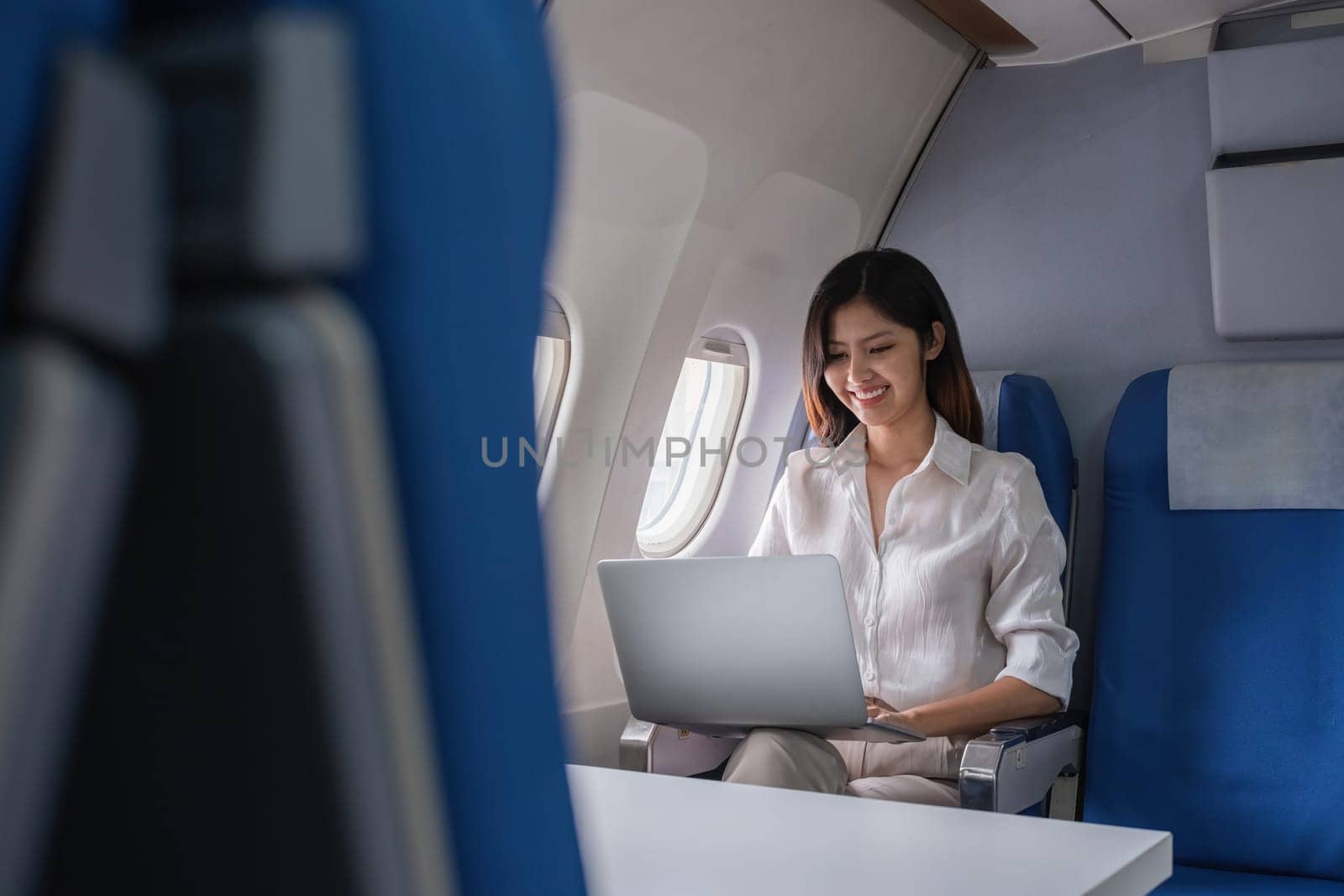 Young woman working on laptop during flight on airplane. Concept of travel and remote work.