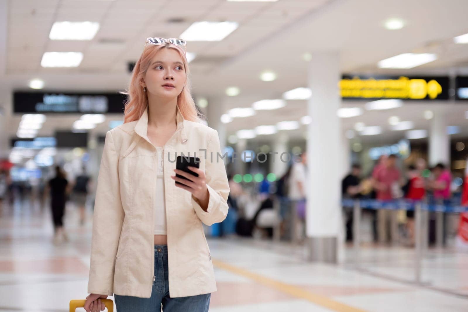 Young traveler with smartphone and luggage at airport terminal. Concept of modern travel, anticipation, and navigation.