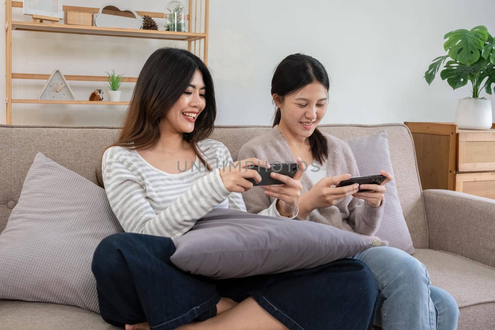 Two young women playing games on smartphones together at home. Concept of friendship and technology.