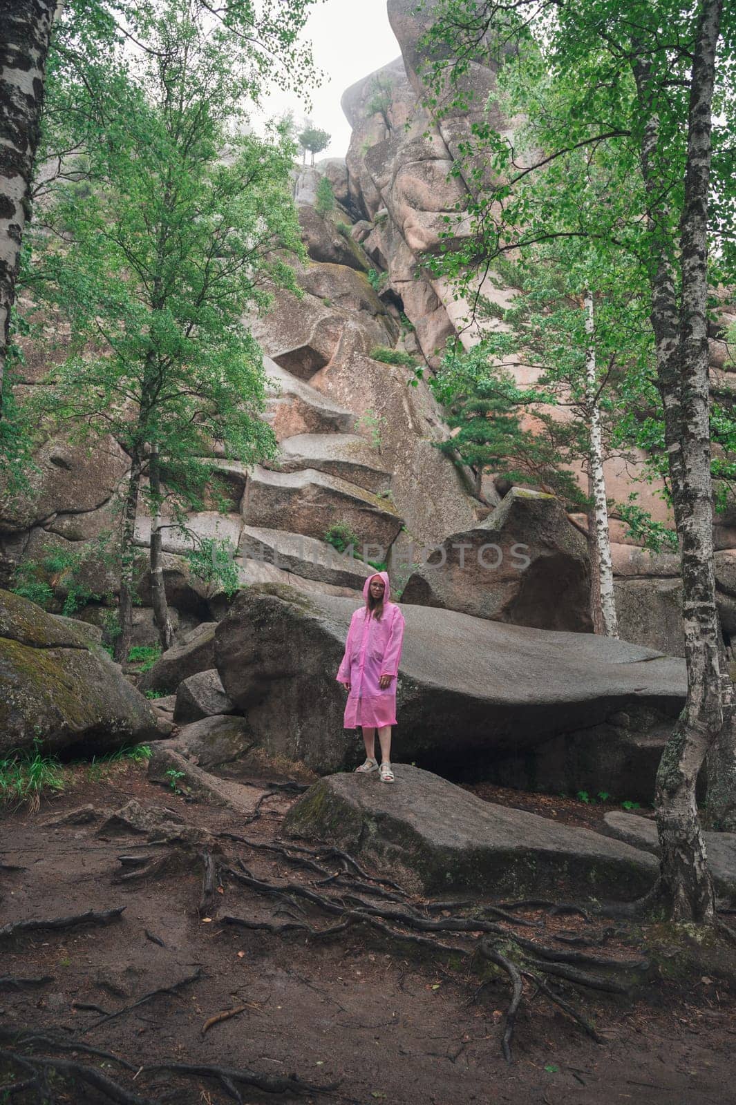 Woman in raincoat in the taiga forest and rocks of the Stolby nature reserve park, Krasnoyarsk, Russia