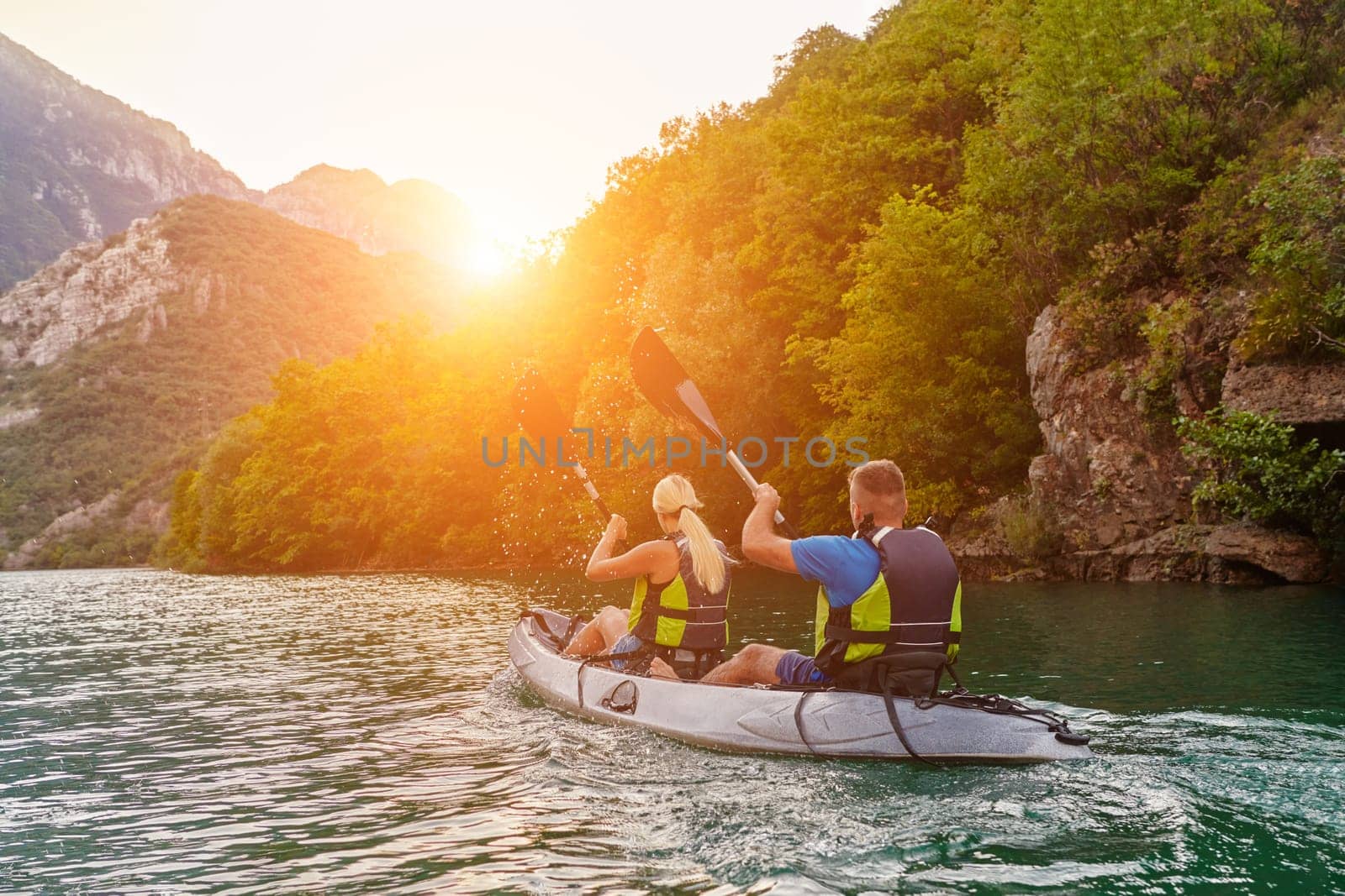 A group of friends enjoying fun and kayaking exploring the calm river, surrounding forest and large natural river canyons during an idyllic sunset