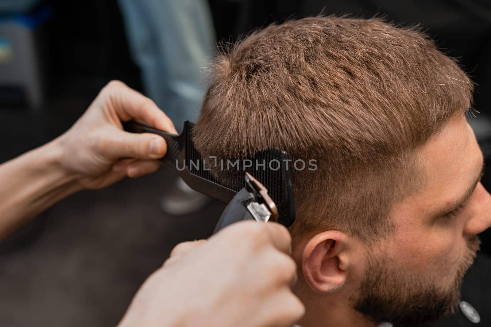 Barber precisely shaves the clients hair with an electric trimmer in the modern barbershop.