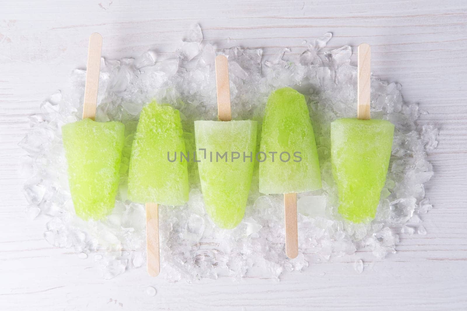 Homemade popsicles with lime juice and mint, mojito fruit ice on a white wooden table.