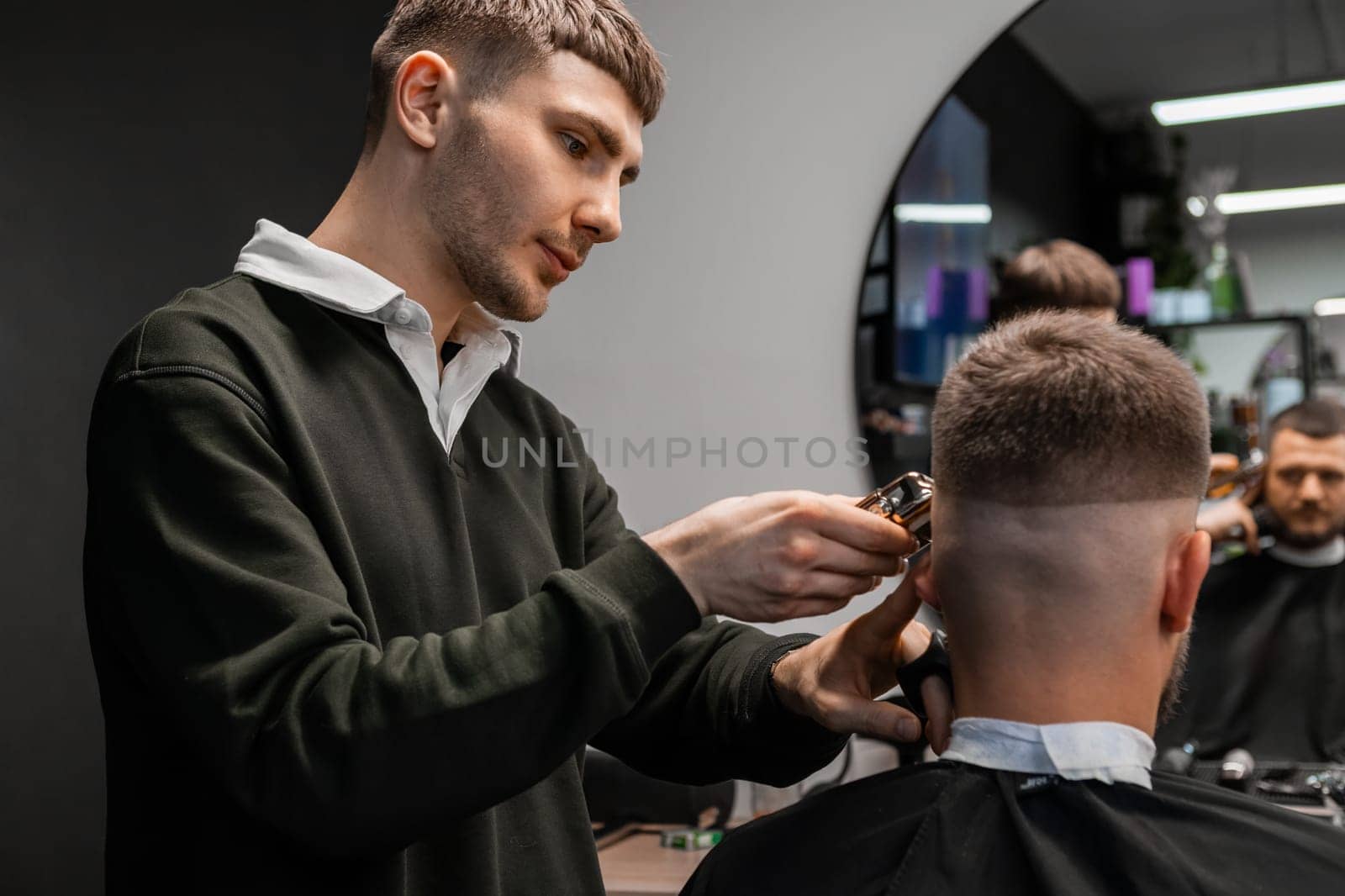 Young barber meticulously cuts the mans hair with a trimmer in the barbershop