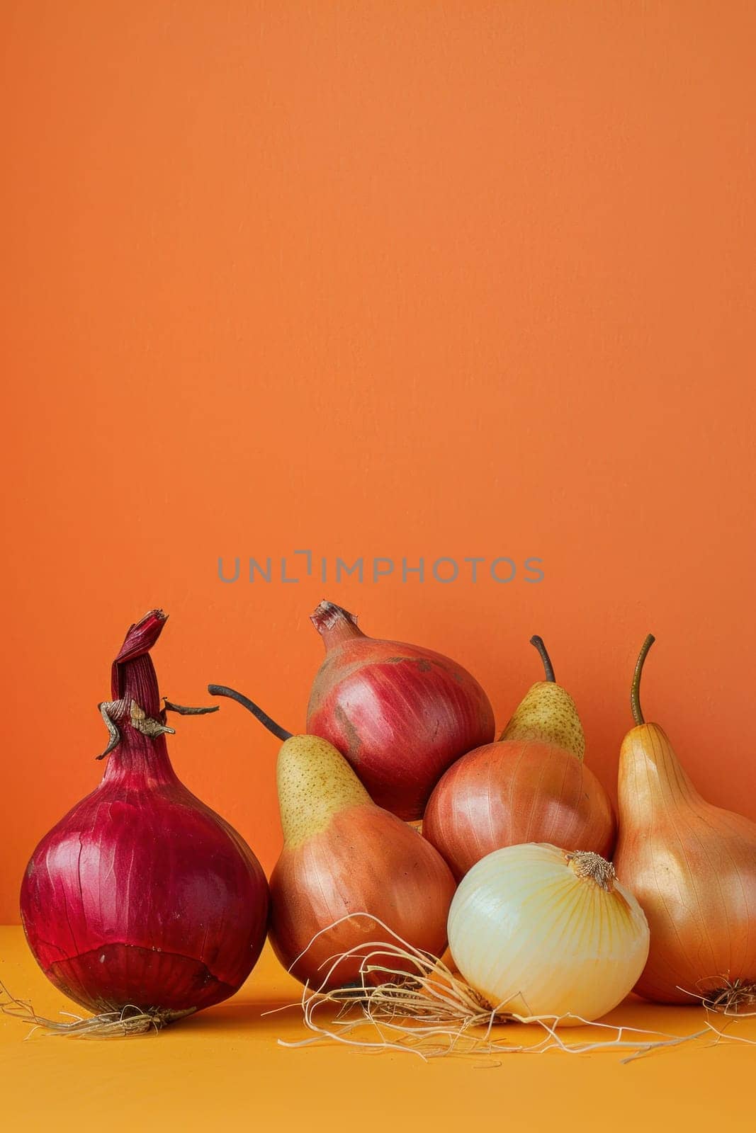 Fresh harvest of onions and pears on vibrant orange background with textural orange wall in background