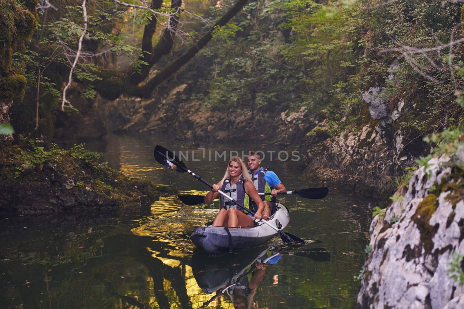 A young couple enjoying an idyllic kayak ride in the middle of a beautiful river surrounded by forest greenery.