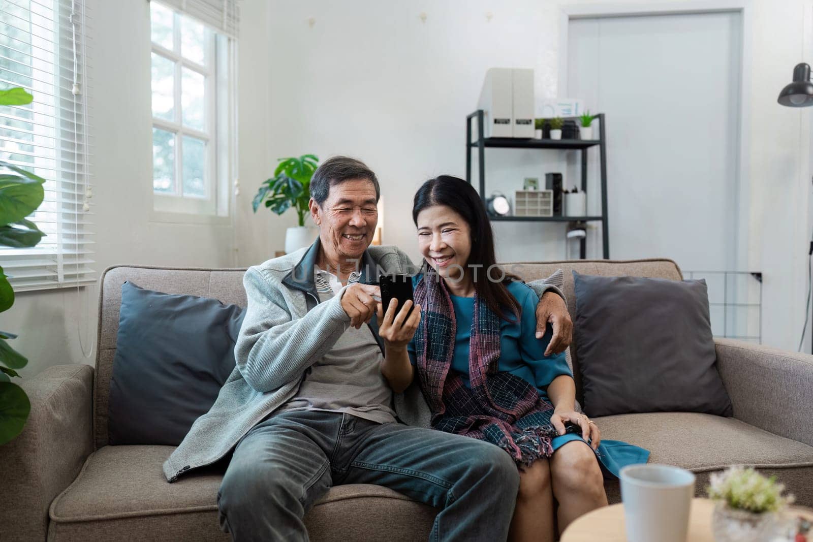 A man and woman are sitting on a couch, both looking at a cell phone. They seem to be enjoying their time together