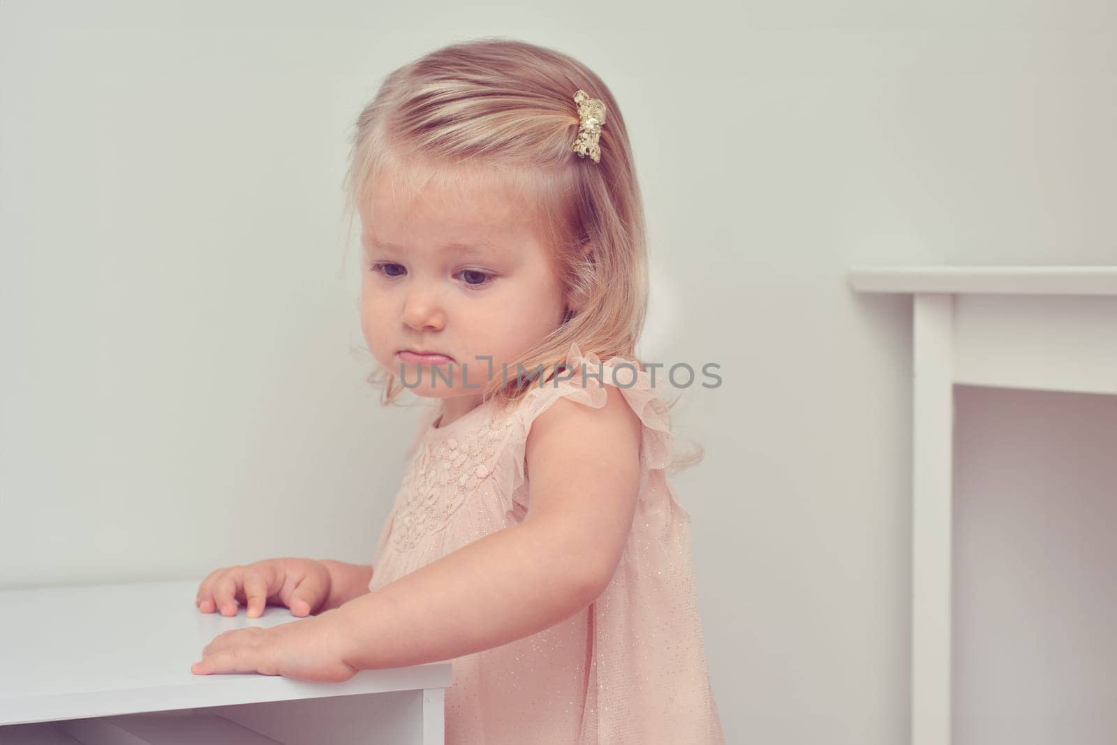 A two-year-old girl in a pink tulle dress in a children's room