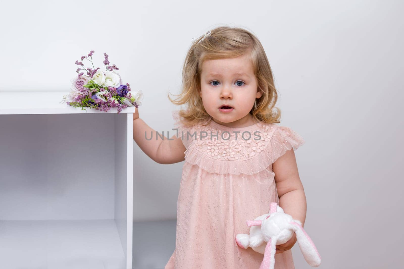 A two-year-old girl with the blue eyes in a pink tulle dress in a children's room