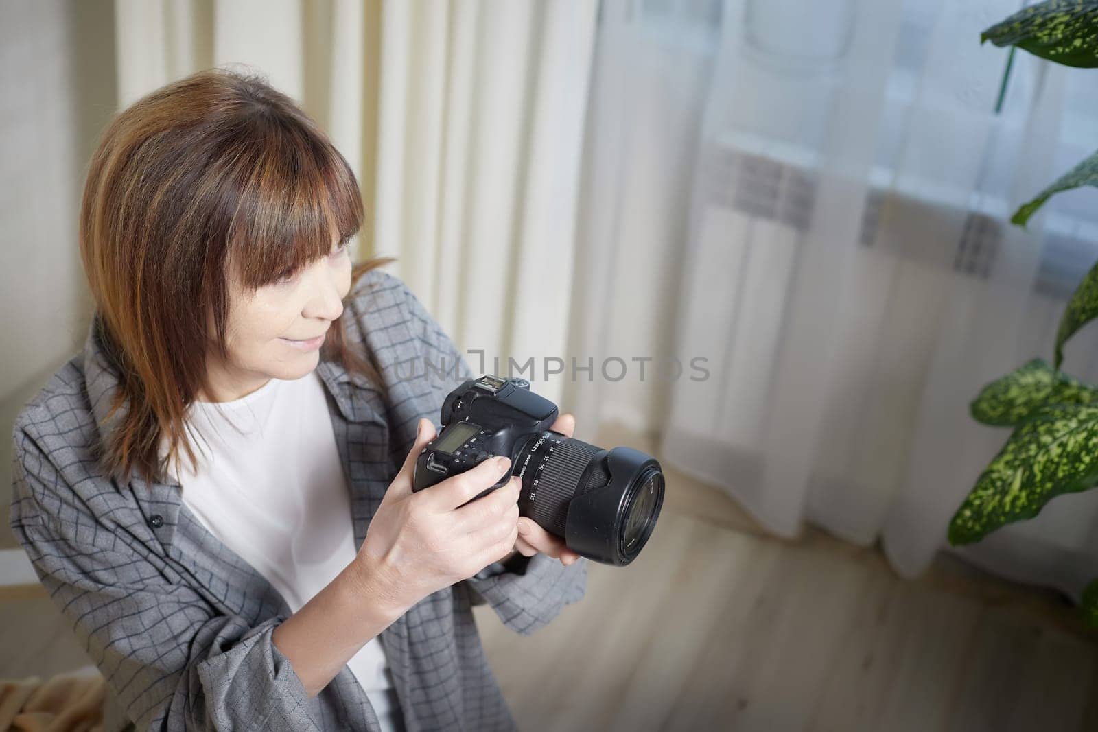 Senior old elderly woman with black camera with a large lens indoors in the studio. Professional photographer. Age Hobby