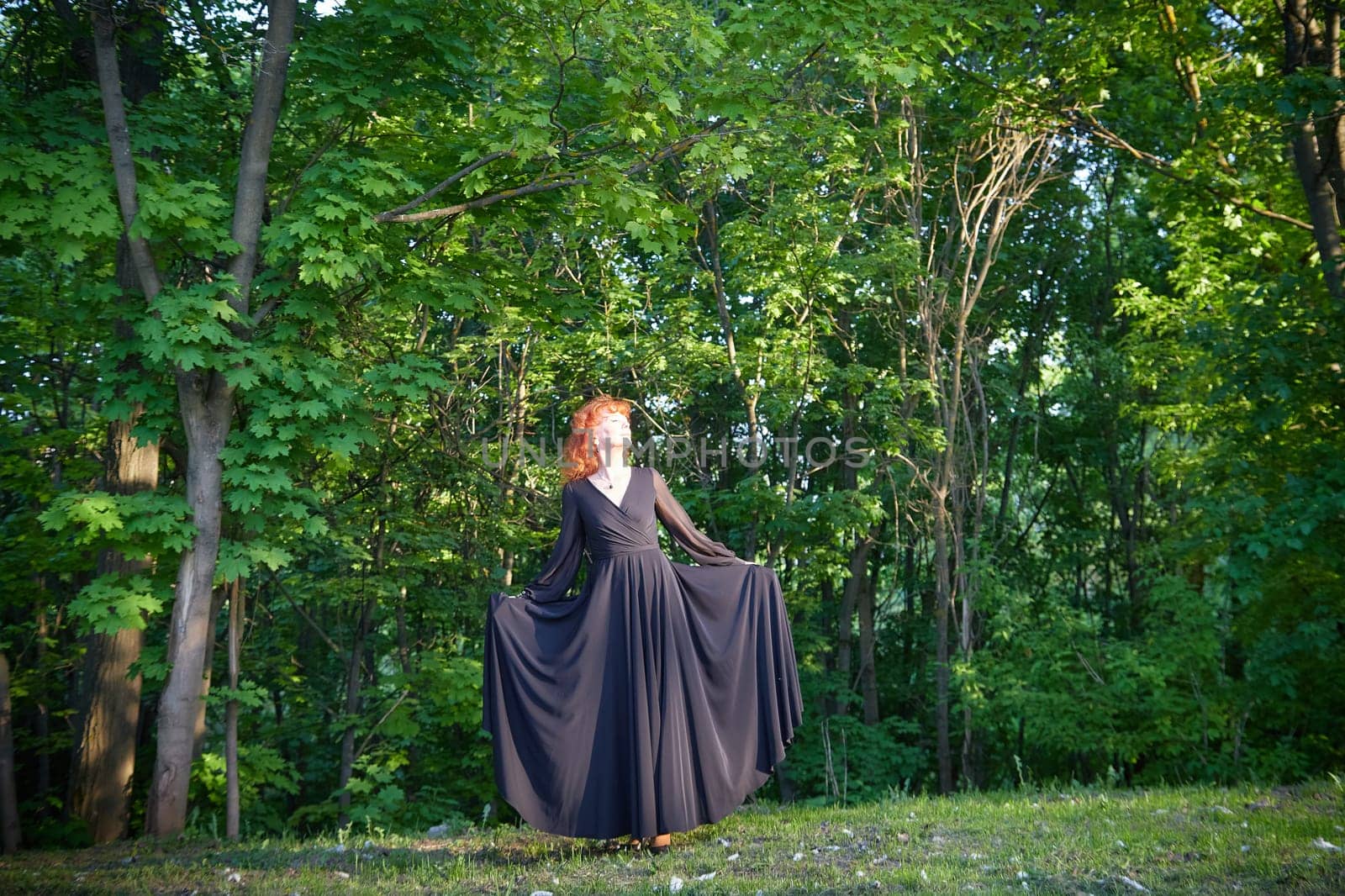 Elegant senior mature Woman dancing in Black Dress in green park. Woman with red hair posing on nature