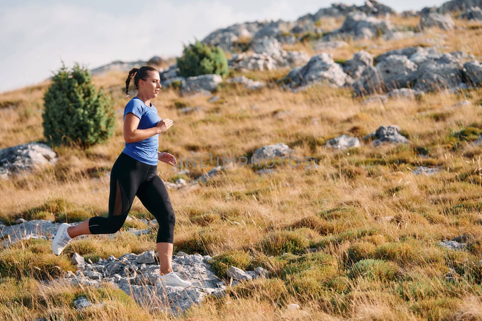 A determined female athlete runs through a forest trail at sunrise, surrounded by breathtaking natural beauty and vibrant greenery.