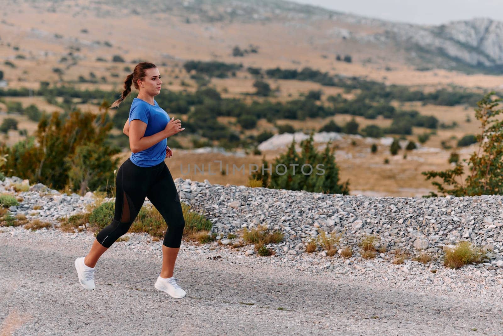 A determined female athlete runs through a forest trail at sunrise, surrounded by breathtaking natural beauty and vibrant greenery.