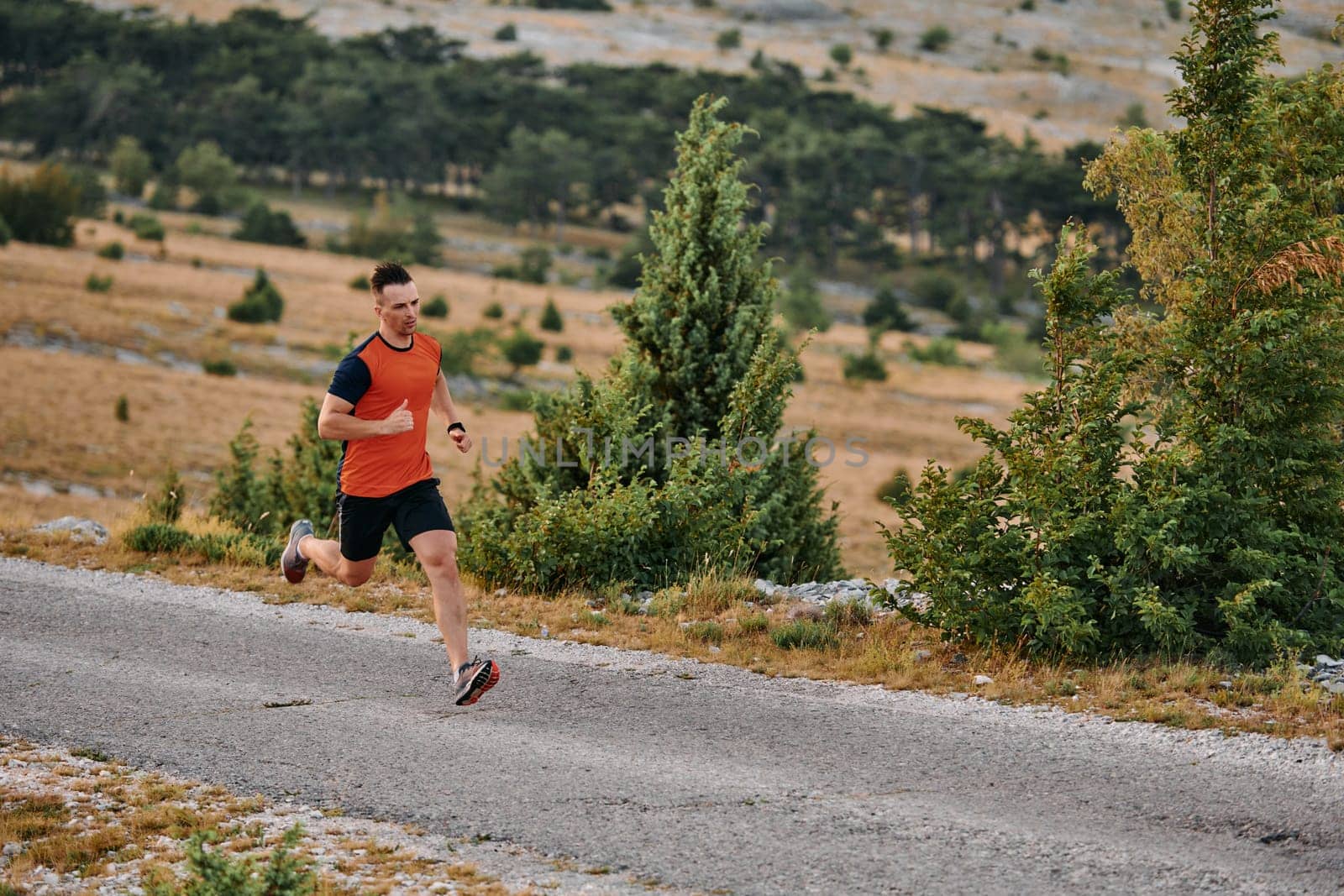 A muscular male athlete runs along a rugged mountain path at sunrise, surrounded by breathtaking rocky landscapes and natural beauty.