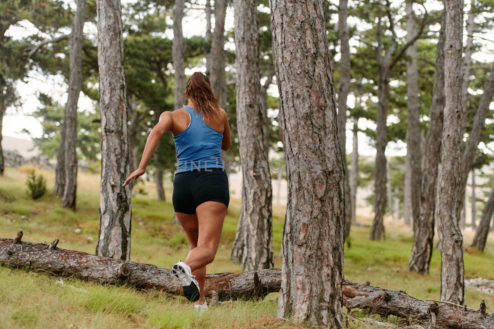 An intrepid woman fearlessly navigates through perilous forest terrain, effortlessly leaping over wooden obstacles with determination and grace, showcasing her adventurous spirit and athletic prowess