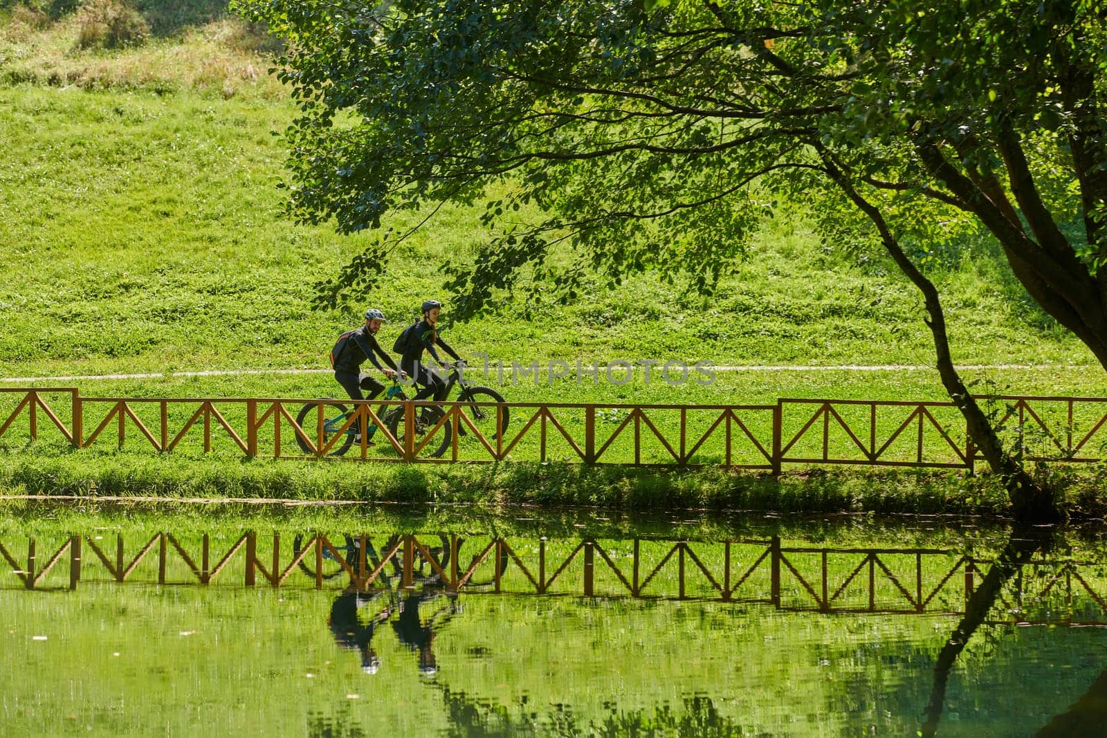 A blissful couple, adorned in professional cycling gear, enjoys a romantic bicycle ride through a park, surrounded by modern natural attractions, radiating love and happiness.