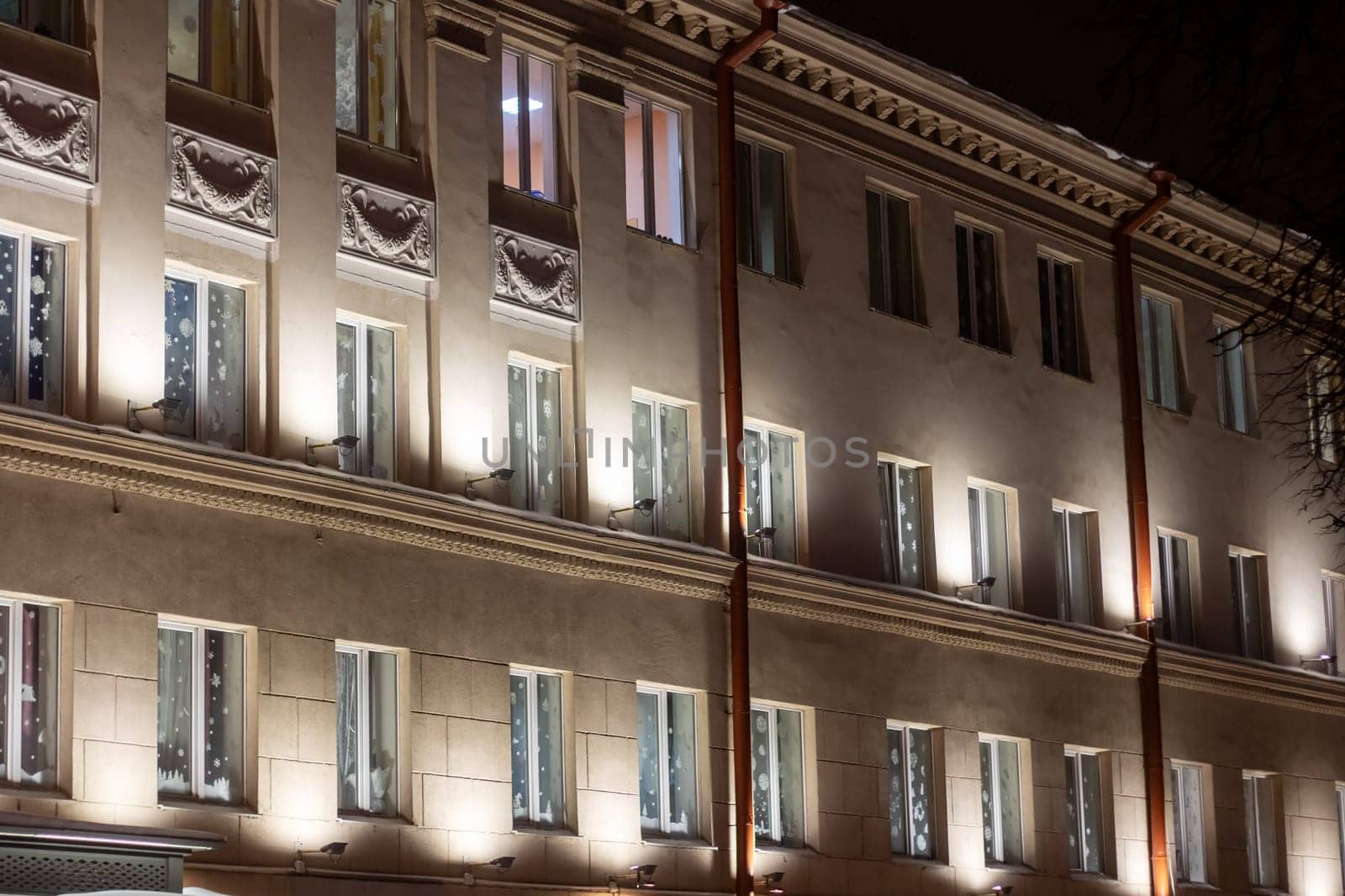 At night, a building with many windows shines brightly, displaying symmetry in its facade, symbolizing the citys metropolis with its unique blend of arches and columns