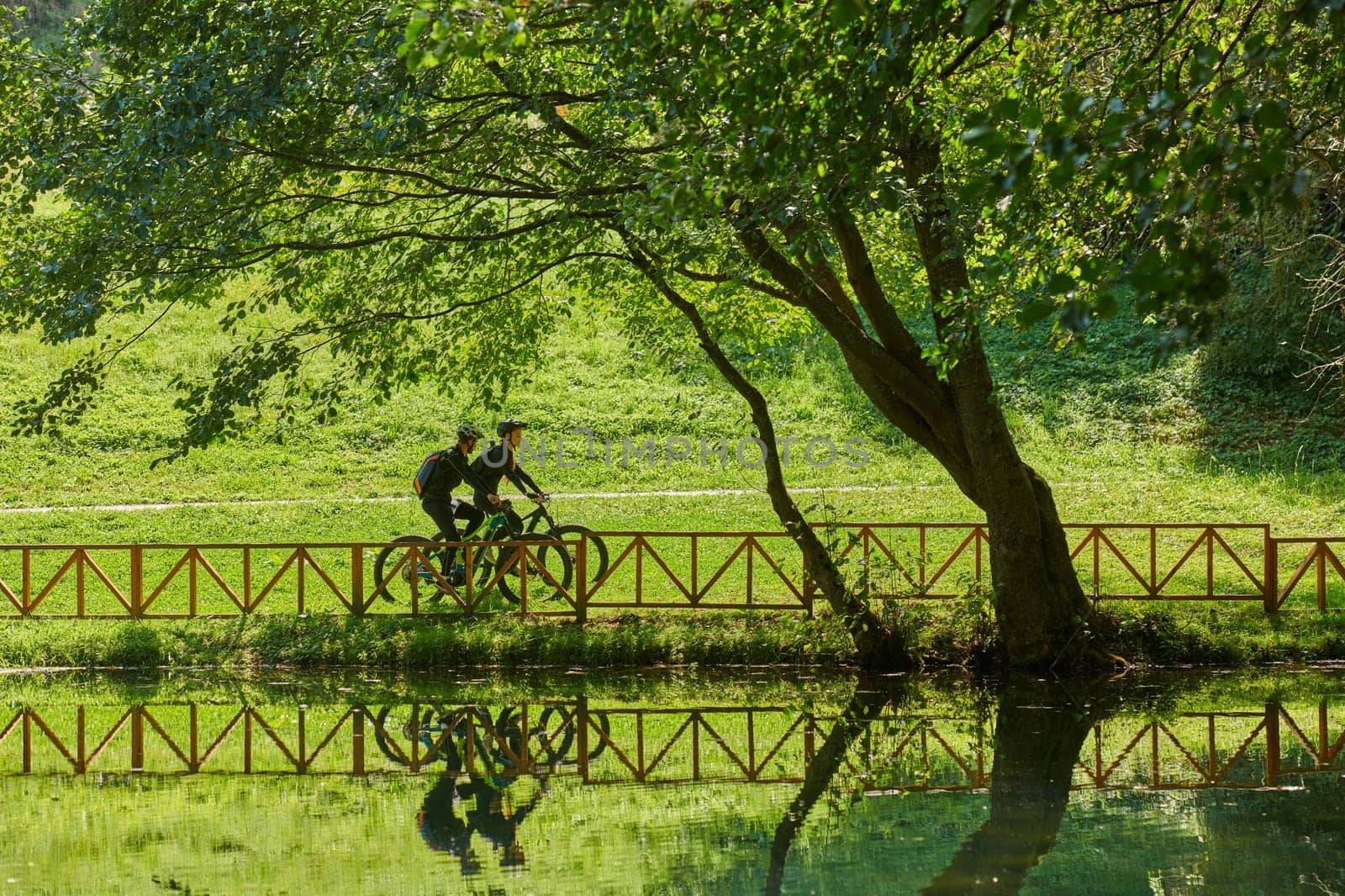 A blissful couple, adorned in professional cycling gear, enjoys a romantic bicycle ride through a park, surrounded by modern natural attractions, radiating love and happiness.